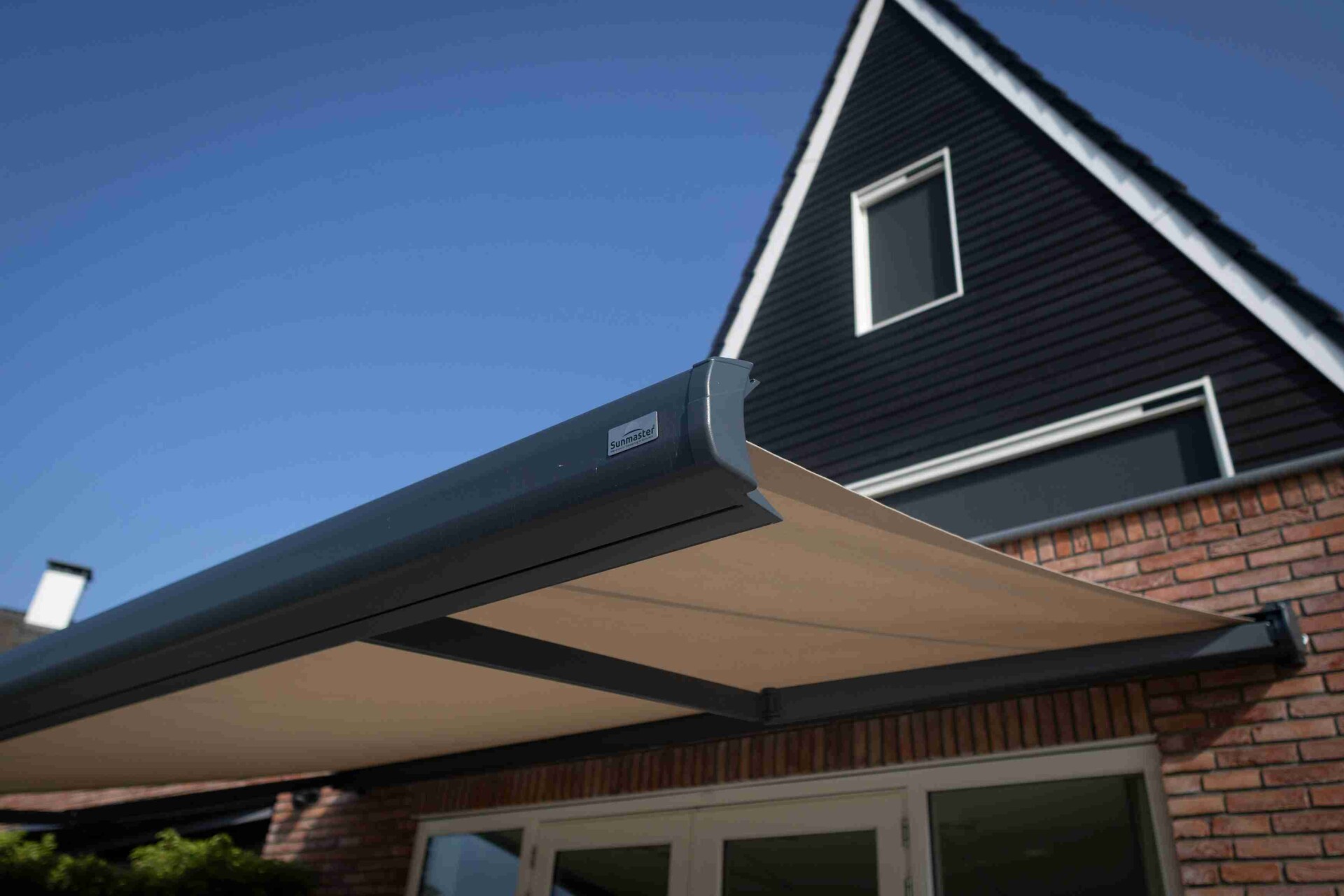 Close up van Sunmaster terrasscherm met antraciet cassette en licht doek boven tuindeuren aan een bakstenen gevel